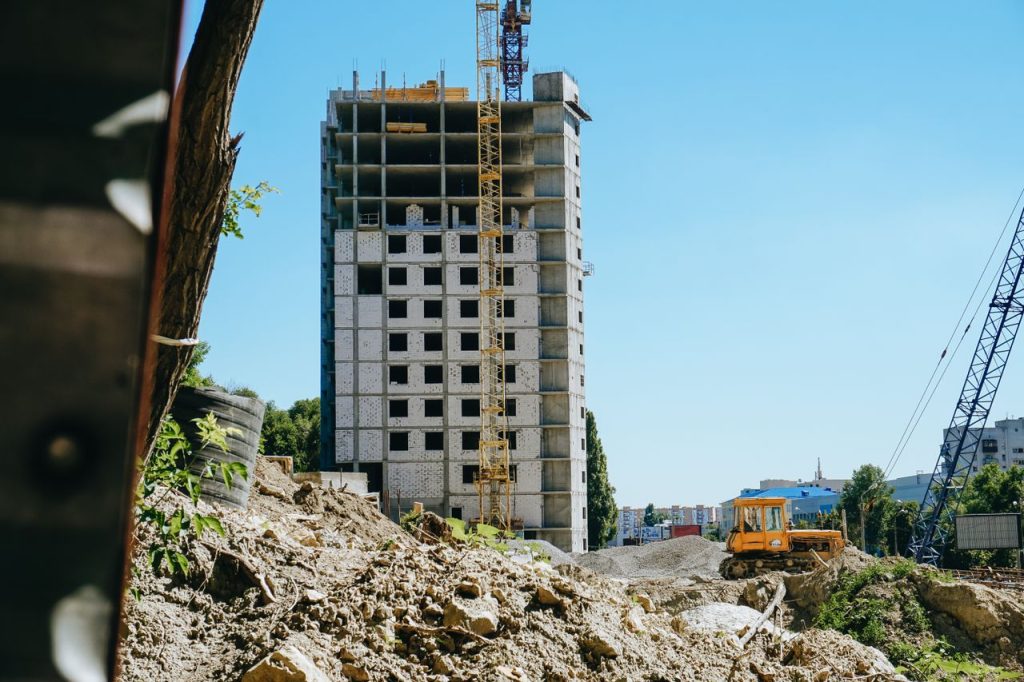 Mid-rise building under construction with cranes and machinery in a cityscape.